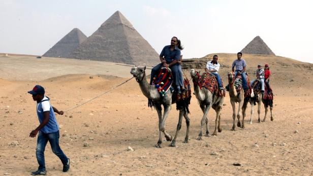 Eine Gruppe von Touristen reitet auf Kamelen vor den Pyramiden von Gizeh.