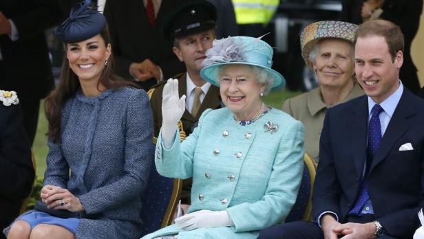Königin Elisabeth II. winkt, während Kate Middleton und Prinz William daneben sitzen.