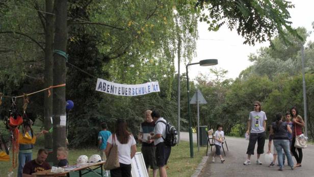 Eine Gruppe von Menschen versammelt sich vor einem Banner mit der Aufschrift „Abenteuerschule AT“.