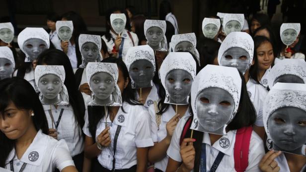 Schülerinnen halten Masken mit dem Gesicht eines Mädchens und leeren Augenhöhlen hoch.