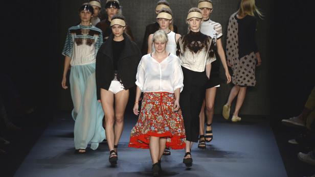 Eine Modenschau mit einer Designerin und mehreren Models auf dem Laufsteg.