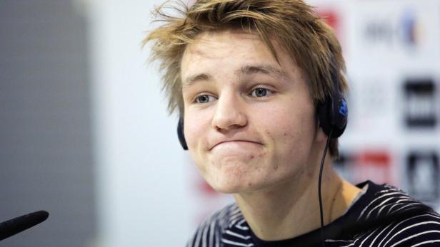 Ein junger Mann mit blonden Haaren und Kopfhörern blickt leicht grinsend zur Seite.