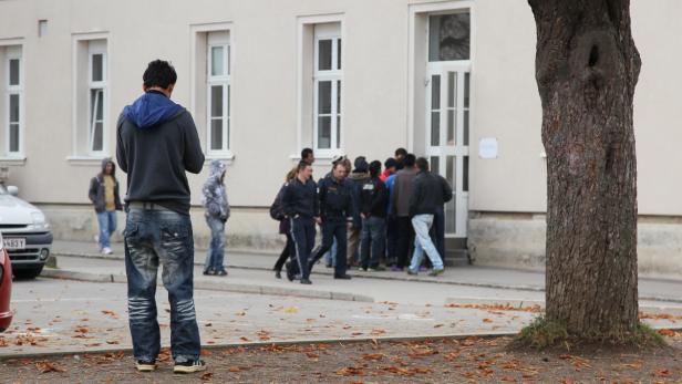 Eine Gruppe von Menschen steht vor einem Gebäude, bewacht von einem Polizisten.