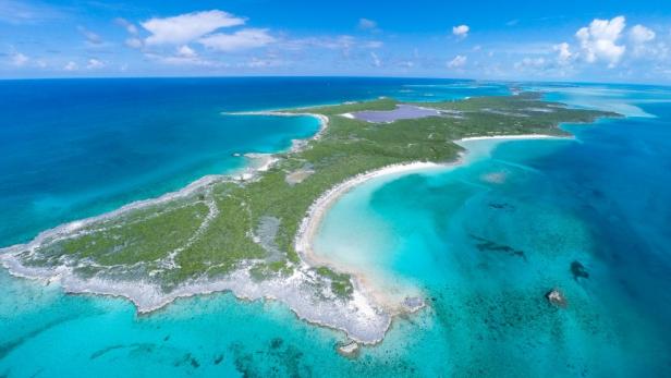 Luftaufnahme einer tropischen Insel mit türkisfarbenem Wasser und grüner Vegetation.