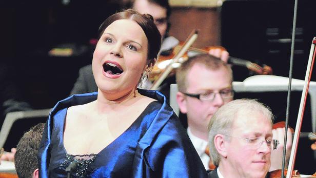Eine Opernsängerin singt mit einem Orchester im Hintergrund.