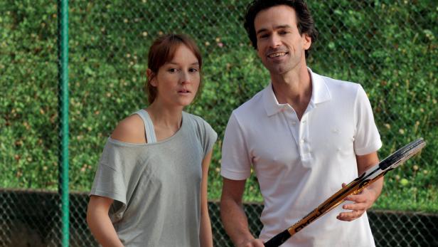 Ein Mann mit Tennisschläger und eine Frau stehen auf einem Tennisplatz.