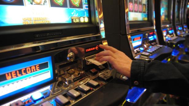 Eine Hand führt eine Banknote in einen Spielautomaten ein.