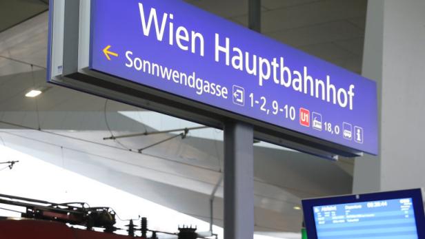 Ein Wegweiser zum Wiener Hauptbahnhof mit einem Zug im Hintergrund.