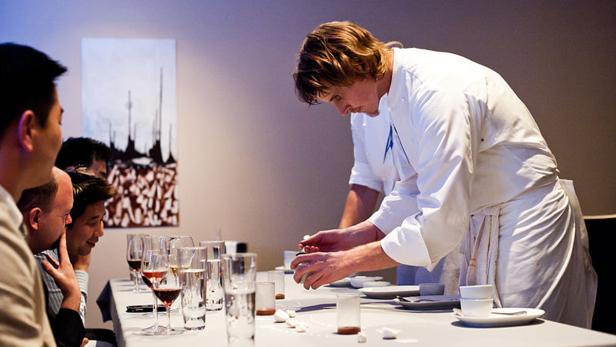 Ein Koch bereitet vor den Augen einer Gruppe von Gästen Speisen zu.