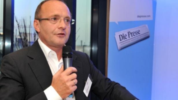 Ein Mann mit Brille spricht in ein Mikrofon vor einem Banner von „Die Presse“.