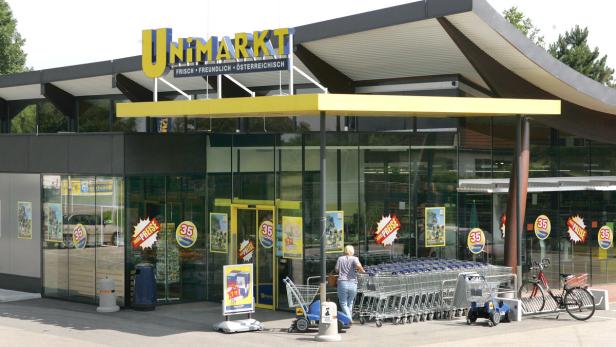Ein Unimarkt-Supermarkt mit Einkaufswagen und Werbeplakaten vor dem Eingang.