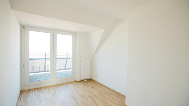 Ein leerer, heller Raum mit Holzboden und Zugang zu einem Balkon.