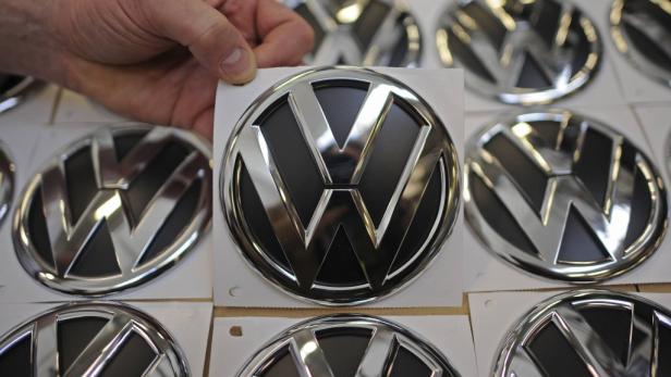 Eine Hand hält ein Volkswagen-Logo, umgeben von weiteren Logos.