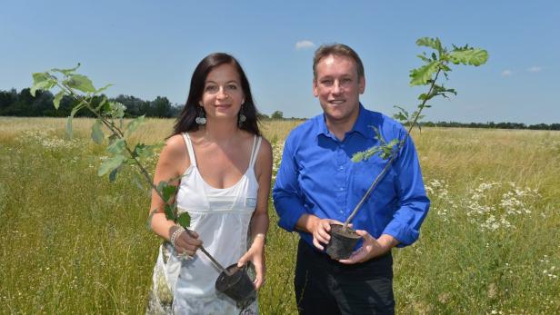 Eine Frau und ein Mann halten jeweils einen kleinen Baum in einem Topf auf einem Feld.