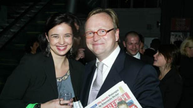 Eine Frau mit einem Weinglas und ein Mann mit einer Zeitung der Marke „Österreich“ posieren für ein Foto.