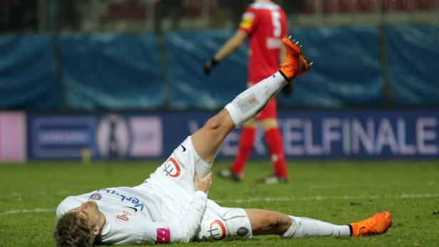 Ein Fußballspieler liegt verletzt auf dem Rasen und hält sich das Bein.