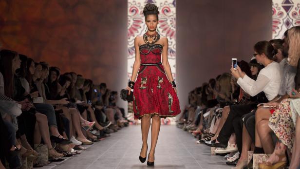 Eine Frau in einem roten Kleid läuft auf dem Laufsteg bei einer Modenschau.