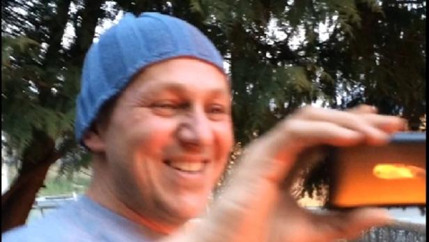 Ein lächelnder Mann mit Mütze filmt mit seinem Smartphone.