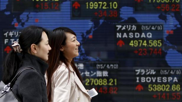 Zwei Frauen gehen an einer Anzeigetafel mit Börseninformationen vorbei.