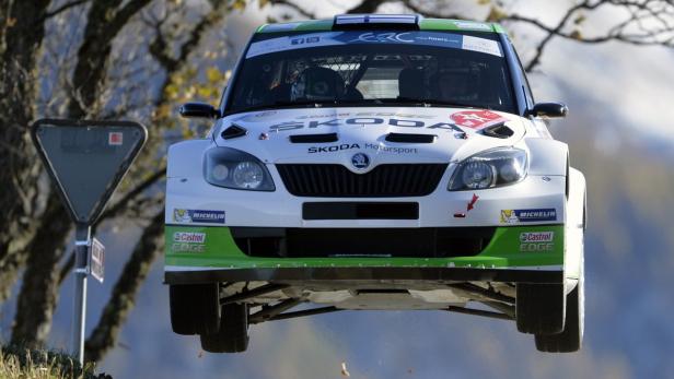 Ein weißer Škoda-Rallyewagen springt über eine Kuppe.