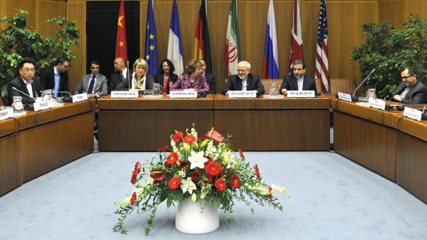Diplomaten sitzen an einem Tisch vor Flaggen verschiedener Nationen.