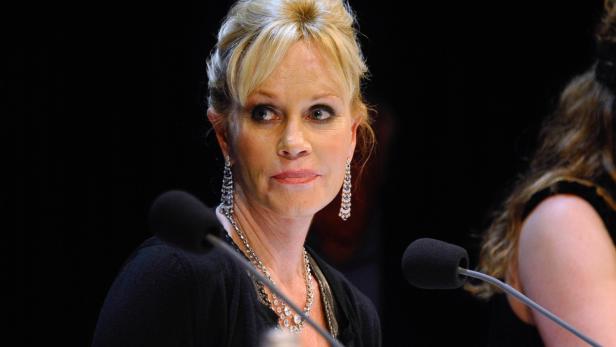 Melanie Griffith bei einer Veranstaltung mit Mikrofonen vor sich.