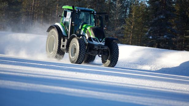 Ein grüner Traktor fährt auf einer schneebedeckten Straße.