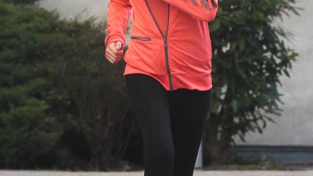 Eine Frau joggt in Sportkleidung über eine Wiese.