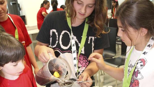 Kinder filtern eine dunkle Flüssigkeit mit einem Sieb.