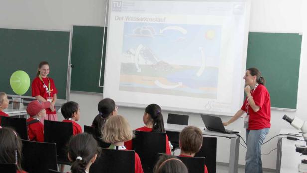 Eine Frau erklärt den Wasserkreislauf vor einer Gruppe von Kindern.