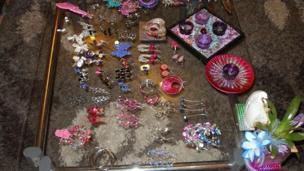 Auf einem Glastisch liegen Schmuck, Haarspangen und dekorative Kerzenhalter.