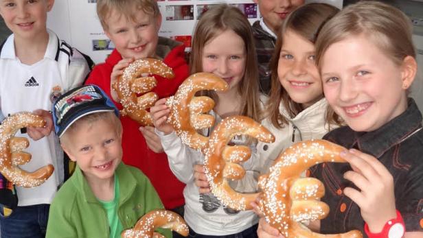 Eine Gruppe Kinder hält Brezeln in Euro-Form in ihren Händen.