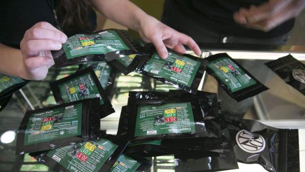 Eine Person hantiert mit mehreren Packungen „Copper Kush“ Cannabisblüten.