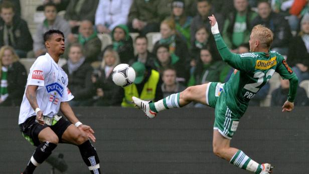 Ein Fußballspieler in Grün schießt den Ball, während ein Gegenspieler in Weiß zusieht.