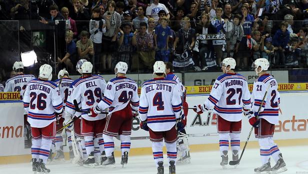 Eishockeyspieler mit Trikots und Rückennummern stehen auf dem Eis vor Zuschauern.