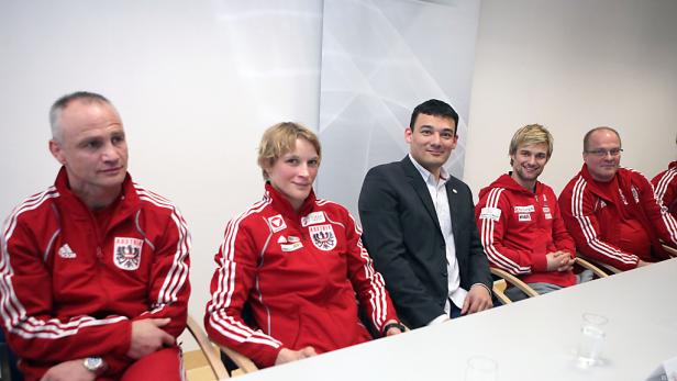 Eine Gruppe von Personen, einige in Trainingsanzügen mit dem österreichischen Wappen, sitzt an einem Tisch.