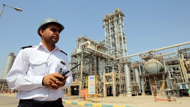 Ein Wachmann mit Funkgerät steht vor einer großen Industrieanlage.