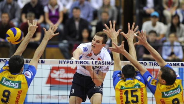 Ein Volleyballspieler schlägt den Ball über das Netz, während gegnerische Spieler versuchen, ihn zu blocken.