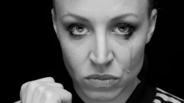 Eine weinende Frau ballt die Faust vor schwarzem Hintergrund.
