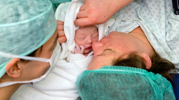 Ein Neugeborenes wird von seiner Mutter und einer medizinischen Fachkraft gehalten.
