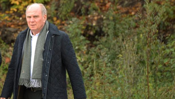 Uli Hoeneß mit Schal und Jacke vor grünem Hintergrund.