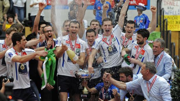 Eine jubelnde Volleyballmannschaft feiert mit Pokal und Champagner ihren Sieg.