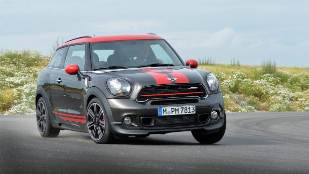 Ein grauer Mini Cooper John Cooper Works mit roten Akzenten auf einer Landstraße.