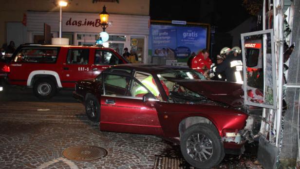 Ein rotes Auto ist in ein Schaufenster gefahren; Rettungskräfte sind vor Ort.