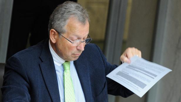 Ein Mann mit Brille und Anzug betrachtet ein Dokument in seiner Hand.