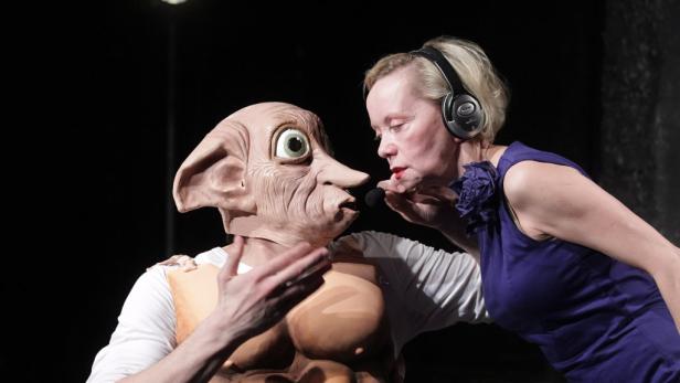 Eine Frau mit Kopfhörern spricht mit einer Person, die eine Dobby-Maske trägt.