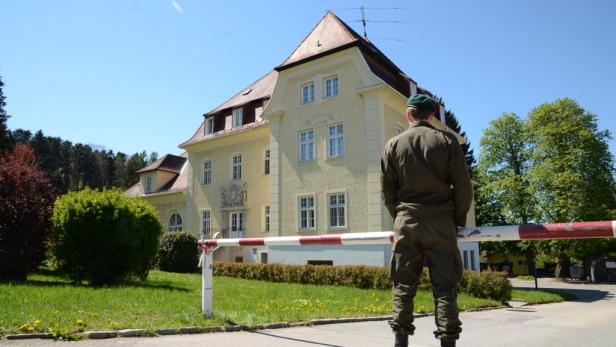 Ein Soldat bewacht ein gelbes Gebäude hinter einer rot-weiß gestreiften Schranke.