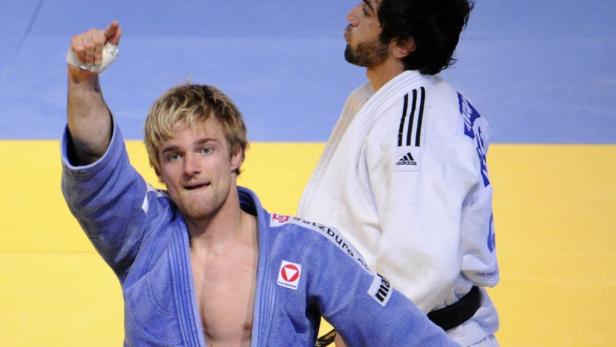 Ein Judoka im blauen Anzug jubelt mit erhobener Faust.