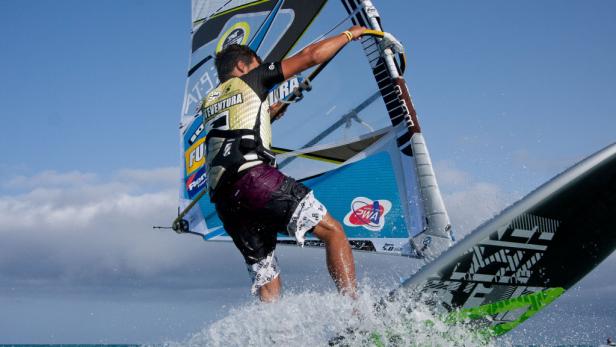 Ein Windsurfer rast mit seinem Segel über das Wasser.