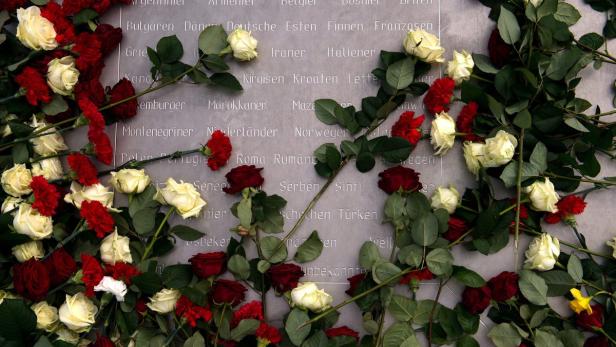 Rote und weiße Rosen liegen vor einer Wand mit eingravierten Nationalitäten.